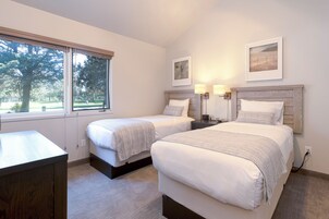 Un dormitorio con dos camas, un escritorio y una ventana con vista a árboles.