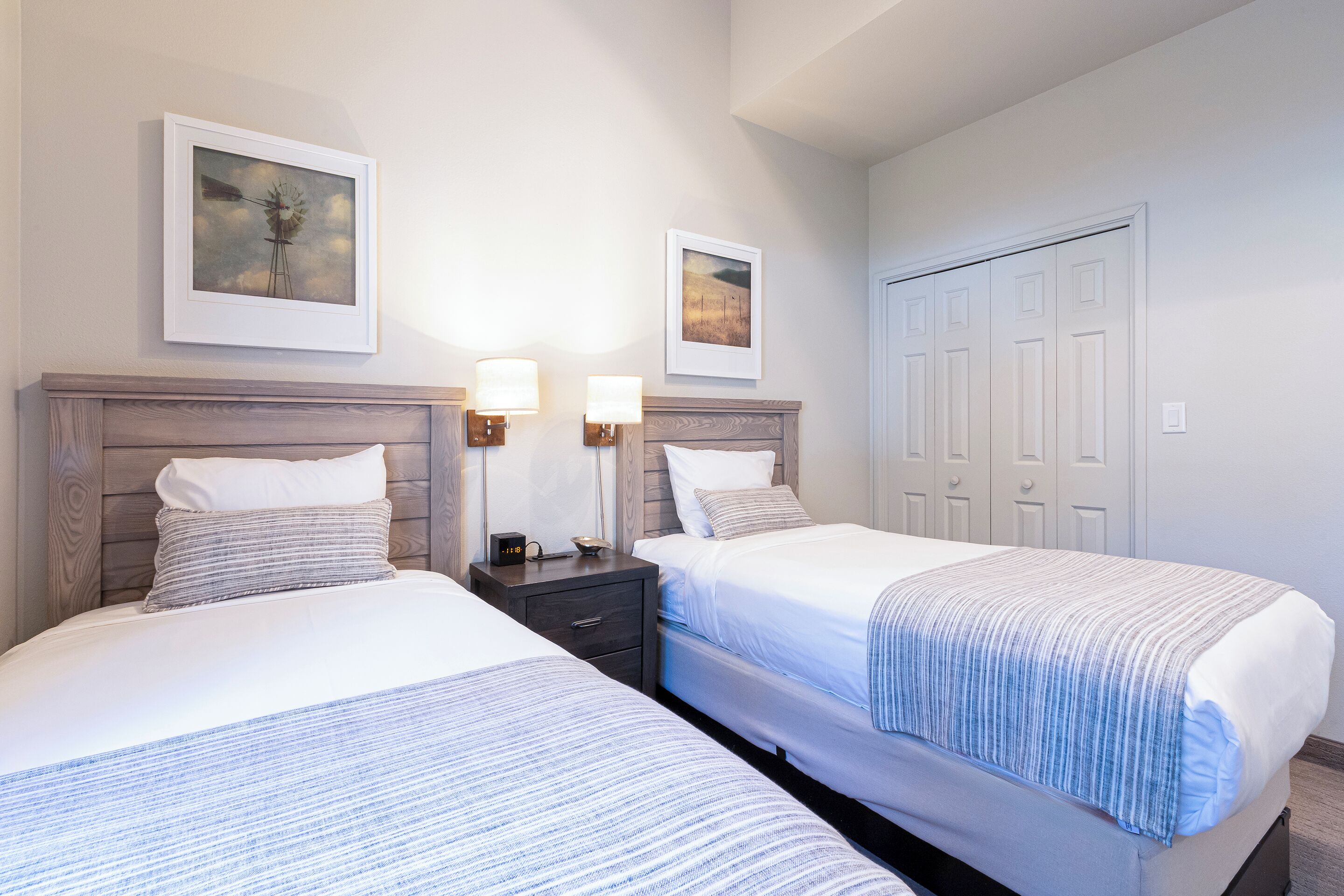 A hotel room with two beds, a wooden headboard, bedside tables with lamps, and framed artwork on the walls.