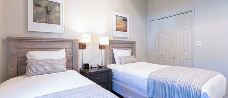 A hotel room with two beds, a wooden headboard, bedside tables with lamps, and framed artwork on the walls.