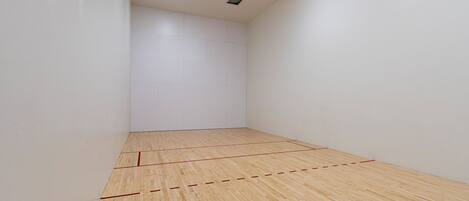 A squash court with white walls and a wooden floor marked with red lines.