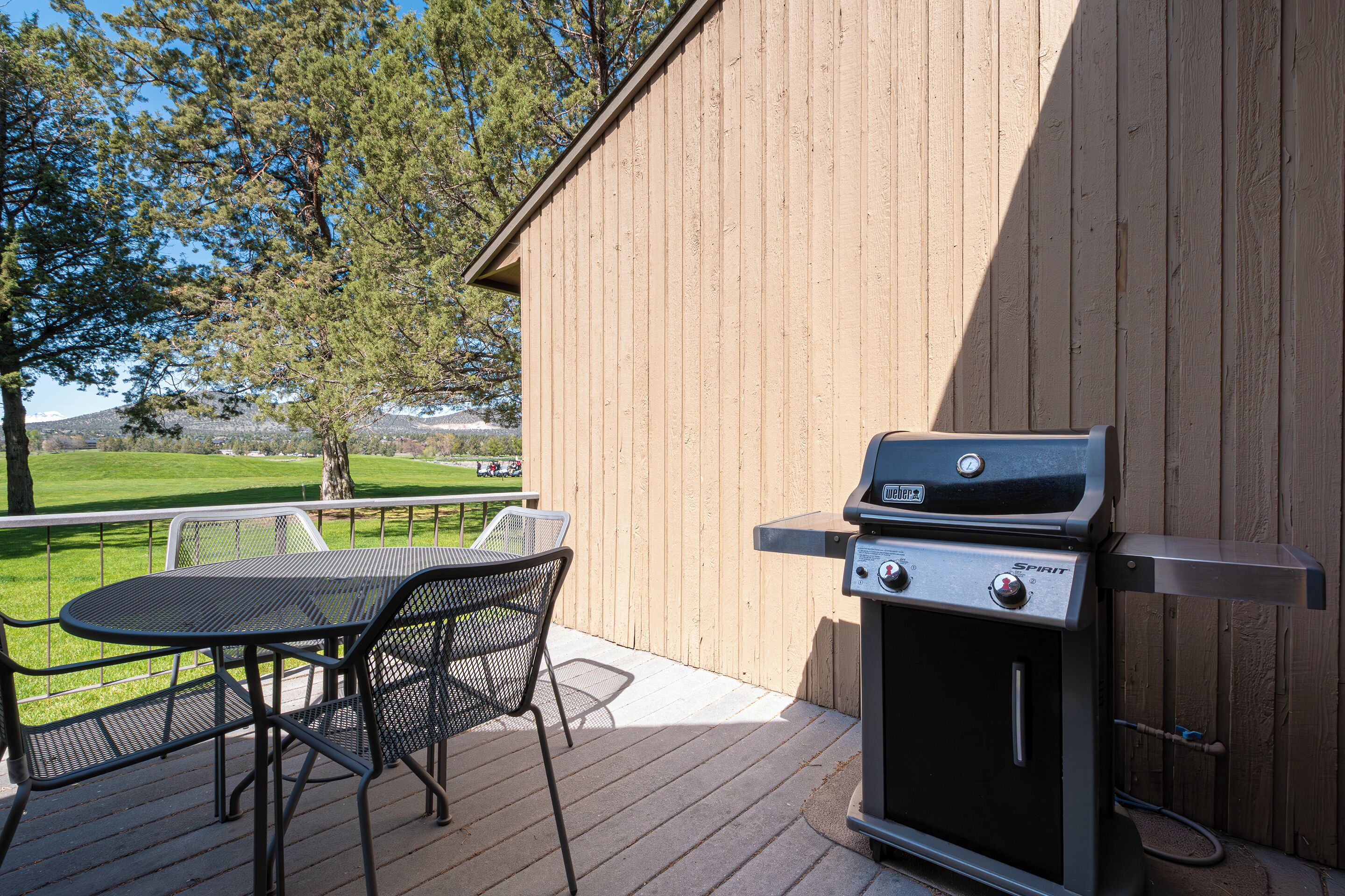 A barbecue grill on a wooden deck with a table and chairs, overlooking a grassy area.