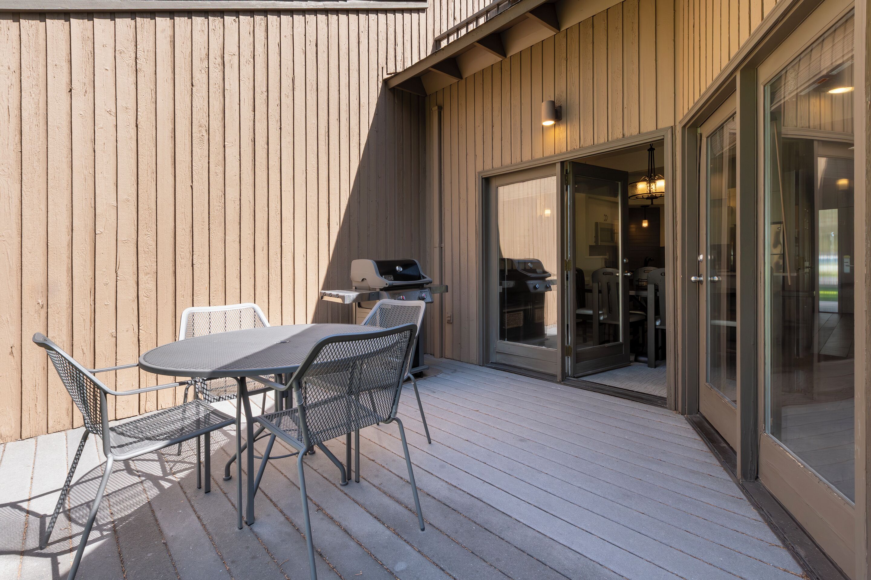 En udendørs patio med et bord, stole, grill og en skydedør ind til et rum.
