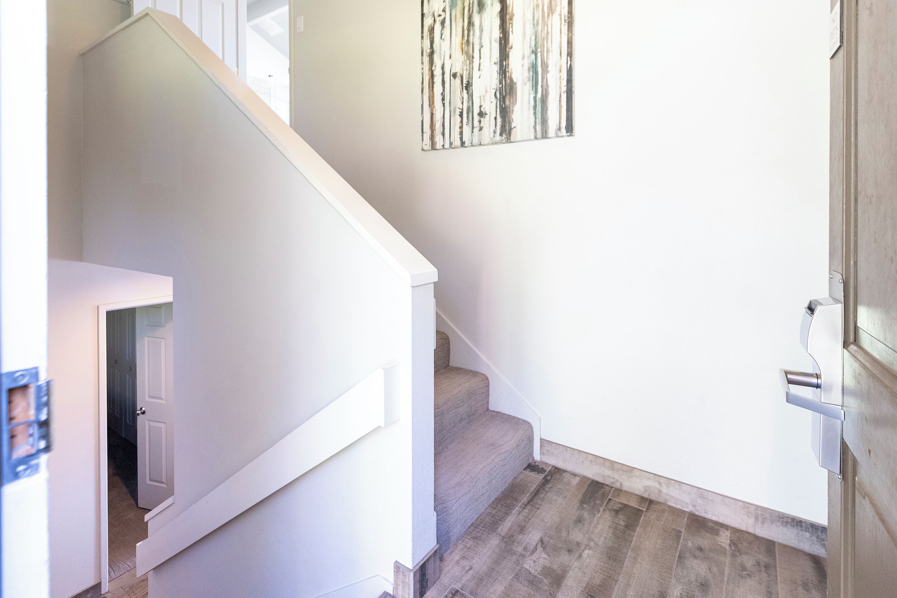 A staircase with a wooden finish, a white wall, and a door leading to another room.