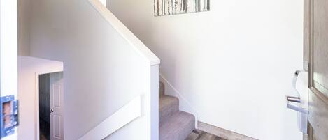 A staircase with a wooden finish, a white wall, and a door leading to another room.