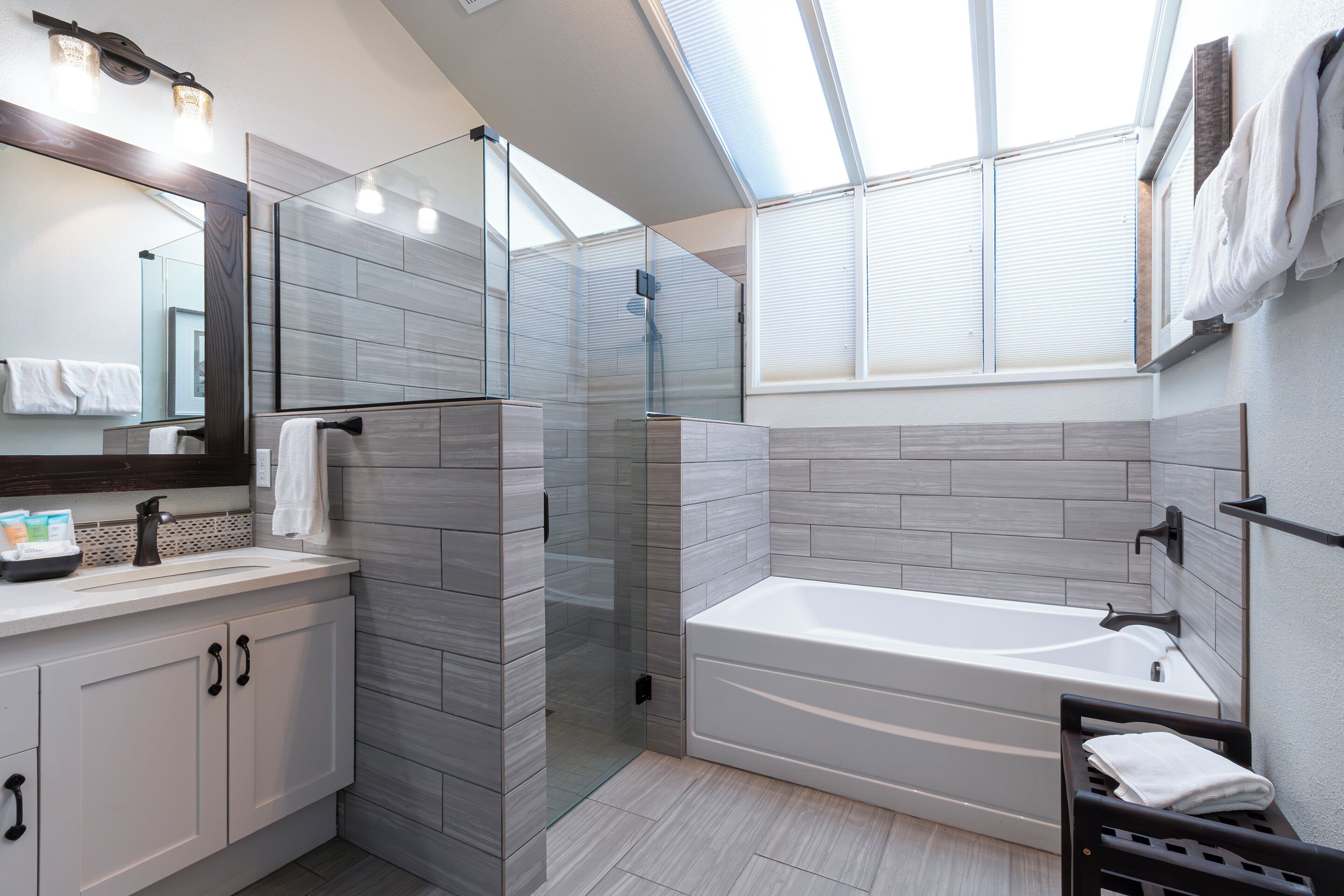 A modern bathroom with a glass-enclosed shower, a large bathtub, and a vanity with a mirror and towel rack.