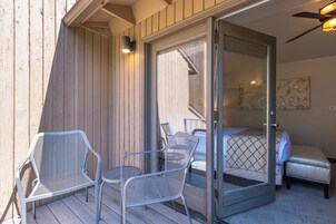 A room with a bed, a sliding glass door, and two metal chairs on a wooden deck.