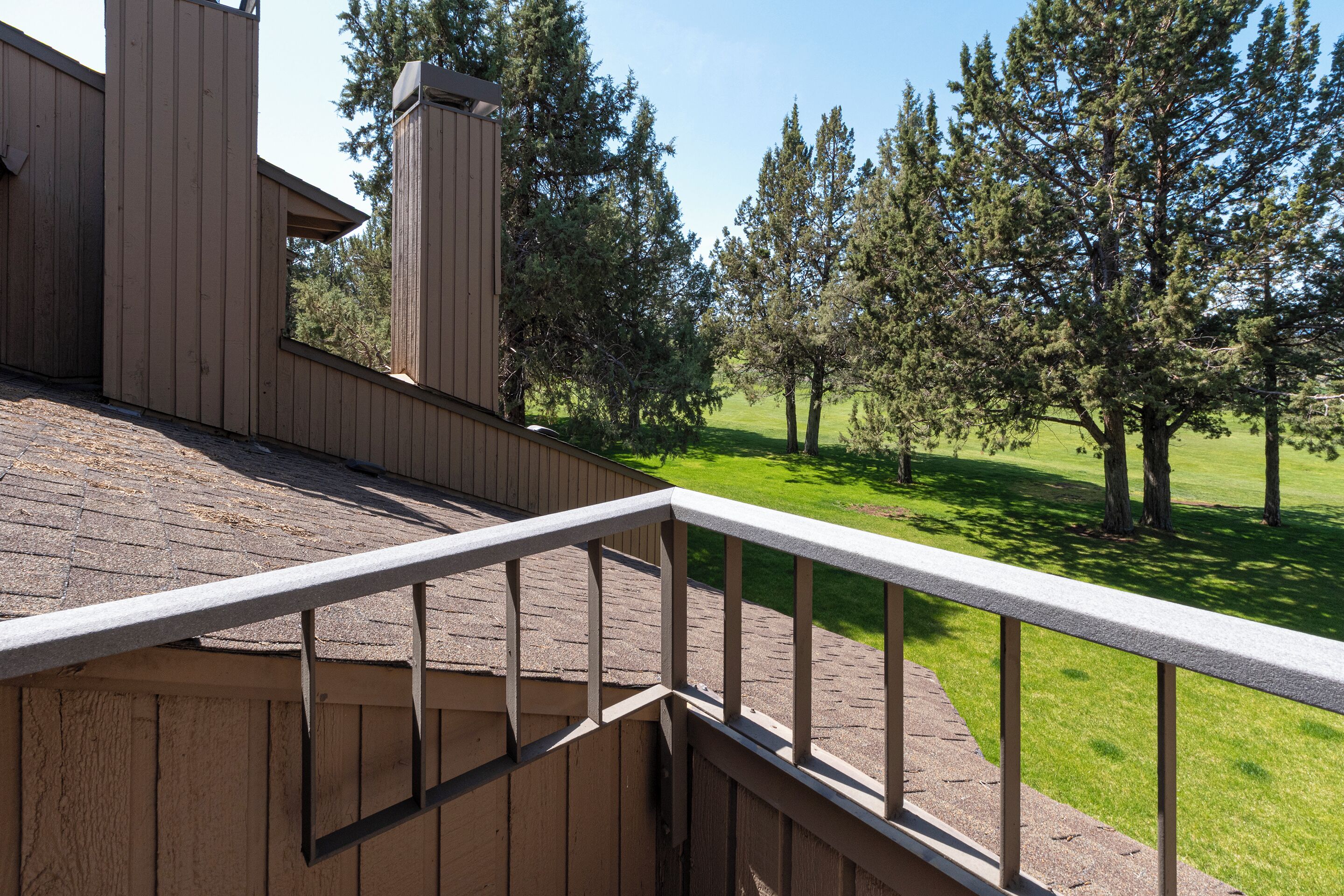 A wooden deck with a metal railing overlooking a grassy area with trees.