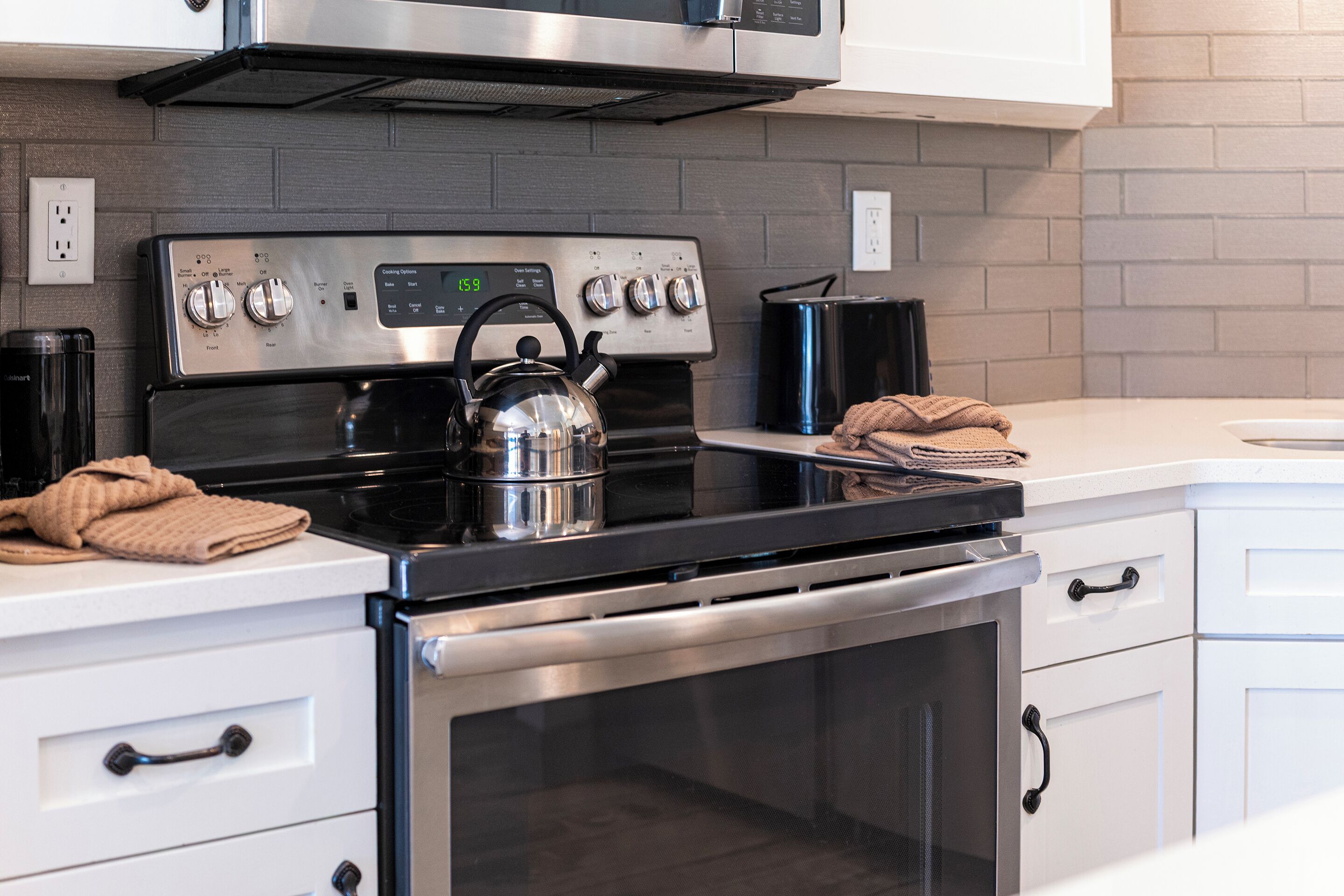 A modern kitchen with stainless steel appliances, a kettle, and a stove.