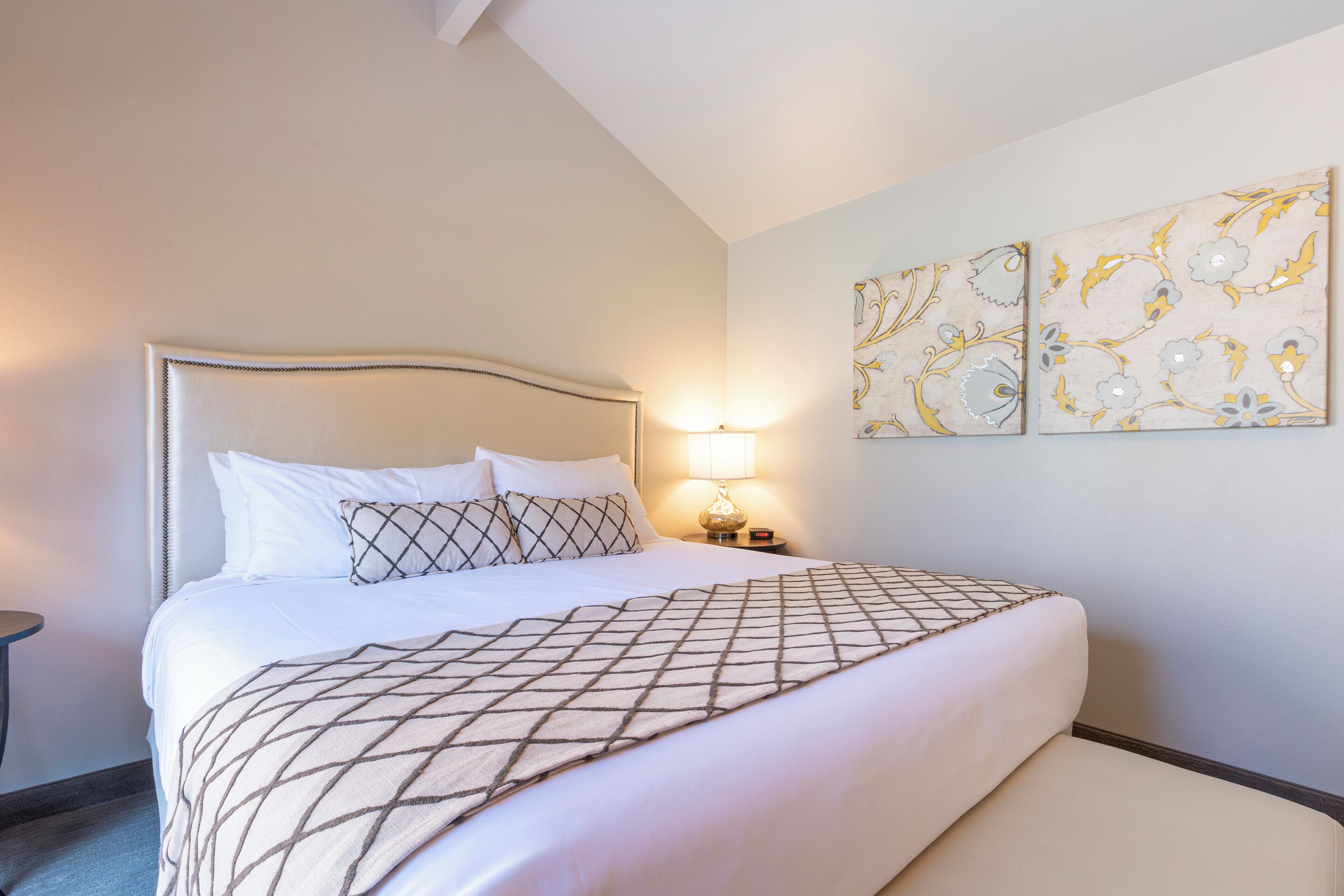 A neatly made bed with a geometric-patterned blanket, a bedside lamp, and two wall-mounted artworks.