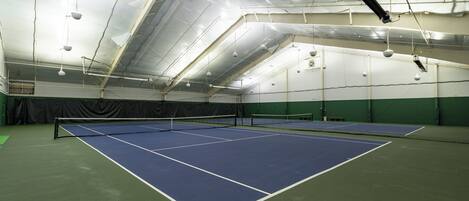 An indoor tennis court with multiple courts, ceiling lights, and a net.