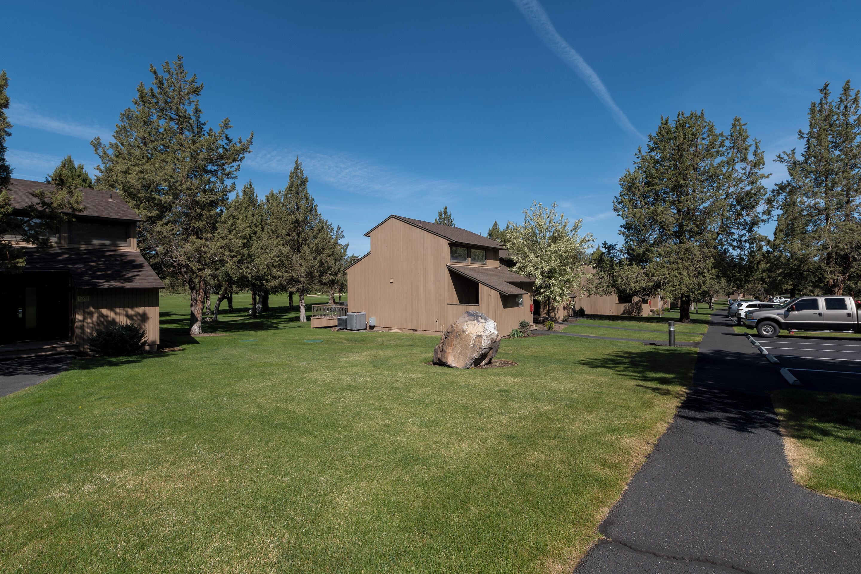 A residential area with houses, a paved walkway, and a large rock in the center.