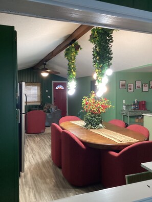 A dining area with a wooden table and red upholstered chairs, a ceiling fan, and hanging plants.