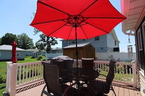 A deck with a red umbrella, wicker furniture, and a white railing.