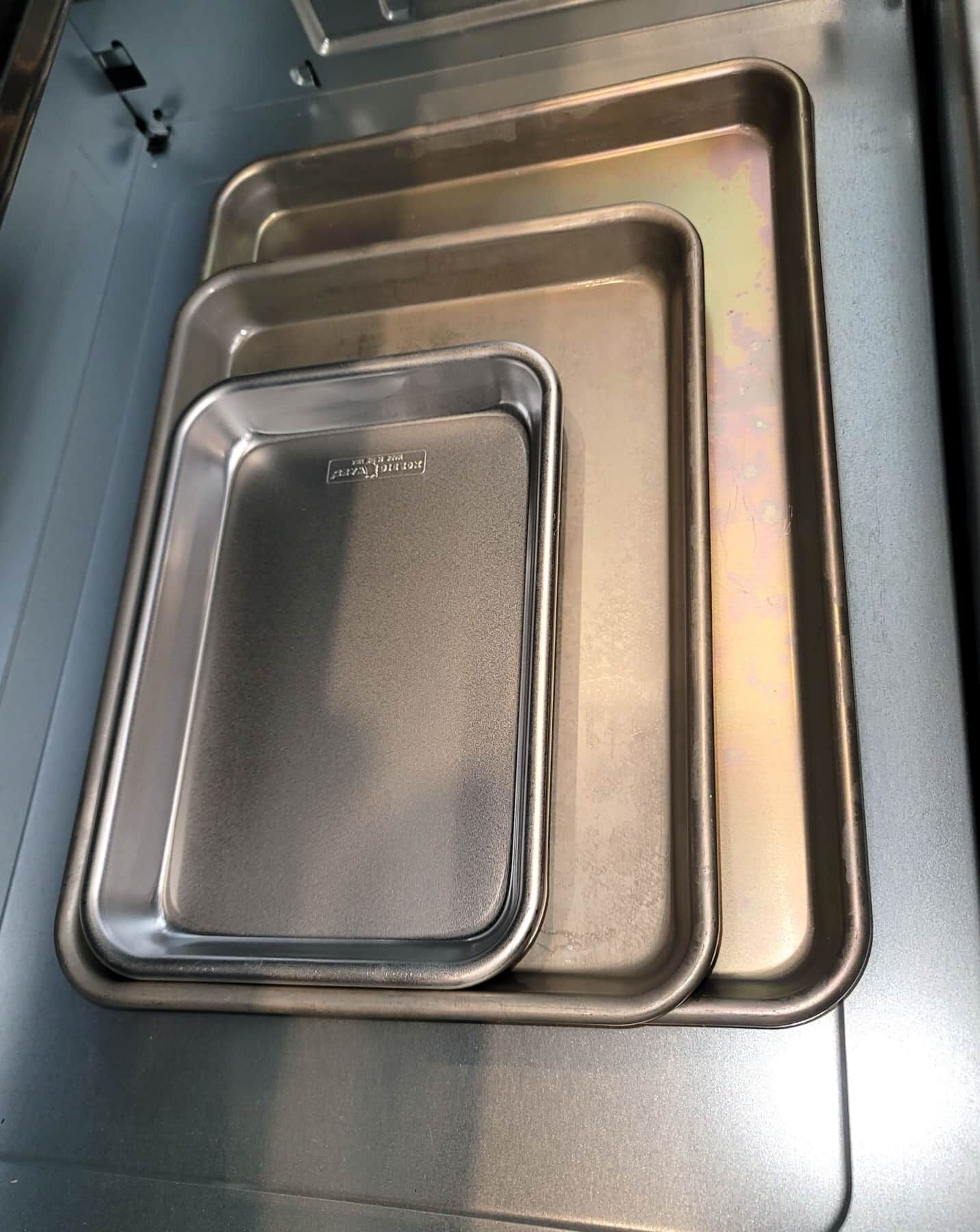 Een roestvrijstalen keuken met twee rechthoekige bakplaten, waarvan één groter is dan de andere, en een spoelgedeelte.