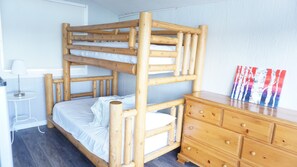 Un lit superposé avec une structure en bois, une table de chevet avec une lampe et une commode avec des tiroirs.