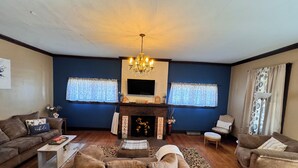 A living room with a fireplace, two sofas, a coffee table, and a chandelier. - Charming Victorian at Lake Shelbyville ⋅ Sleeps 6 ⋅Sunroom ⋅ Fire Pit ⋅ Parking (Shelbyville)