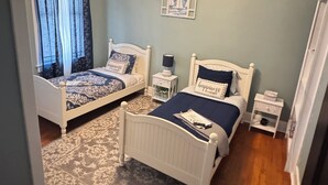 A bedroom with two beds, a ceiling fan, a rug, and a small bedside table with a lamp. - Charming Victorian at Lake Shelbyville ⋅ Sleeps 6 ⋅Sunroom ⋅ Fire Pit ⋅ Parking (Shelbyville)