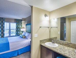 A hotel room with a bed, a bathroom with a sink and mirror, and a window with curtains.