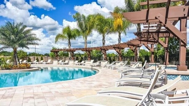 Un área de piscina con sillones de descanso y una pérgola.