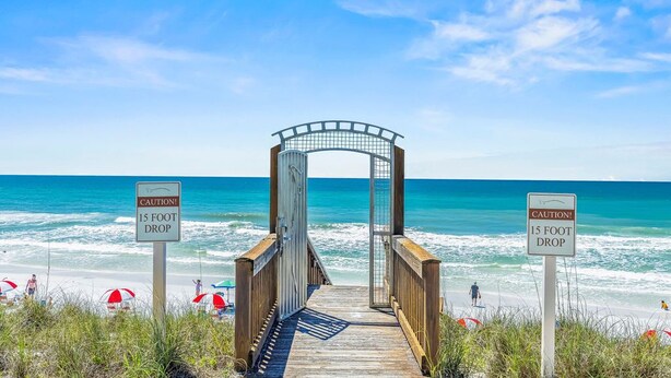 Une promenade en bois mène à une plage, et un panneau d’avertissement indique une falaise d’environ 4,5 mètres de hauteur.