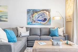 Un salon moderne avec un canapé d’angle gris, une table basse en bois et un grand tableau abstrait accroché au mur.