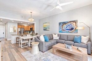 Un salon moderne avec un canapé d’angle gris, une table basse et un coin repas comprenant une table et des chaises blanches.