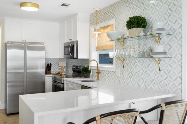 A modern kitchen with white cabinetry, stainless steel appliances, and a glass island.