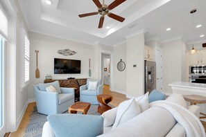 A spacious living room with a ceiling fan, a flat-screen TV, and a kitchen area with modern appliances.