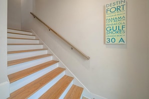 A staircase with wooden steps and a metal handrail, leading to a landing with a wall-mounted sign listing beach destinations.
