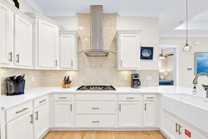 A modern kitchen with white cabinetry, a stainless steel range hood, and a coffee maker.