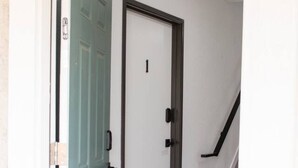 Un pasillo con una puerta verde, una puerta blanca y una escalera a la derecha.