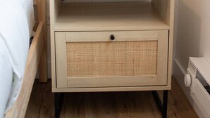 Una mesita de noche de madera con un reloj blanco, una lámpara y una planta en maceta.