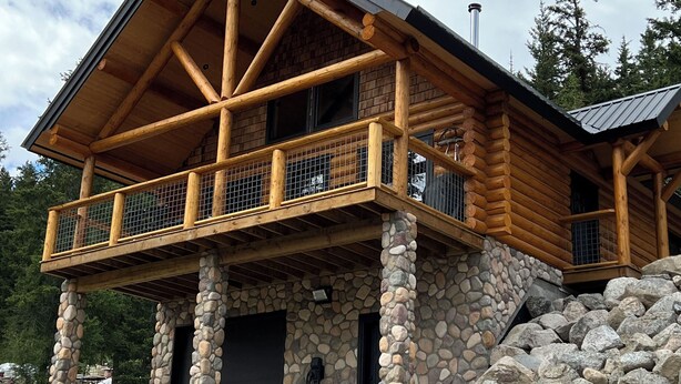 Eine Blockhütte mit Steinunterbau, einem Balkon mit Metallgeländer und einem Schornstein.