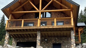 Eine Blockhütte mit Steinunterbau, einem Balkon mit Holzgeländer und einem großen Vordach.
