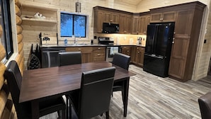 Eine moderne Küche mit Holzschränken, einem schwarzen Kühlschrank und einem Essbereich mit Tisch und Stühlen.