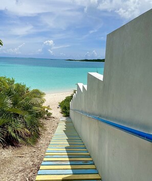 A concrete pathway leading to a beach with clear turquoise water and a distant island. - Extraordinary efficiency apartment w/kitchenette  (Hoopers Bay)