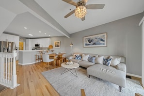 Una sala de estar moderna con un sofá color beige, una mesa de centro y un comedor con una mesa y sillas de madera.
