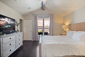 Ein Schlafzimmer mit einem großen Bett, einem Schminktisch, einem Fernseher und einem Fenster mit Vorhängen.