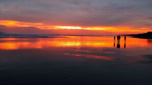 Une plage au coucher du soleil, avec une mer calme et quelques personnes debout sur le rivage.