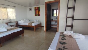 Une chambre d’hôtel avec deux lits en bois, un bureau, une salle de bain avec un miroir et un lavabo, et une fenêtre avec des rideaux légers.