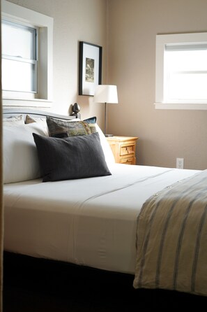 A neatly made bed with a striped blanket, a bedside lamp, and a wooden nightstand with a lamp. - Charming farmhouse suite near Dunedin (Clearwater)