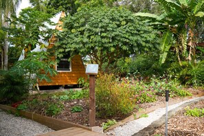 A wooden cabin with a sloped roof, surrounded by a garden with various plants and flowers. - Charming farmhouse suite near Dunedin (Clearwater)
