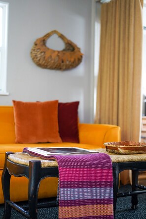 A room with a yellow sofa, a black chair, a woven basket, and a patterned throw on the chair. - Charming farmhouse suite near Dunedin (Clearwater)