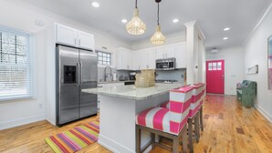A modern kitchen with white cabinets, stainless steel appliances, and a central island with pink and white bar stools. - Blueberry Beach House indoor pool, hot tub (South Haven)