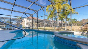Una piscina interna con pareti in vetro trasparente, bordo piastrellato e vista sul territorio circostante, tra cui palme e edifici.