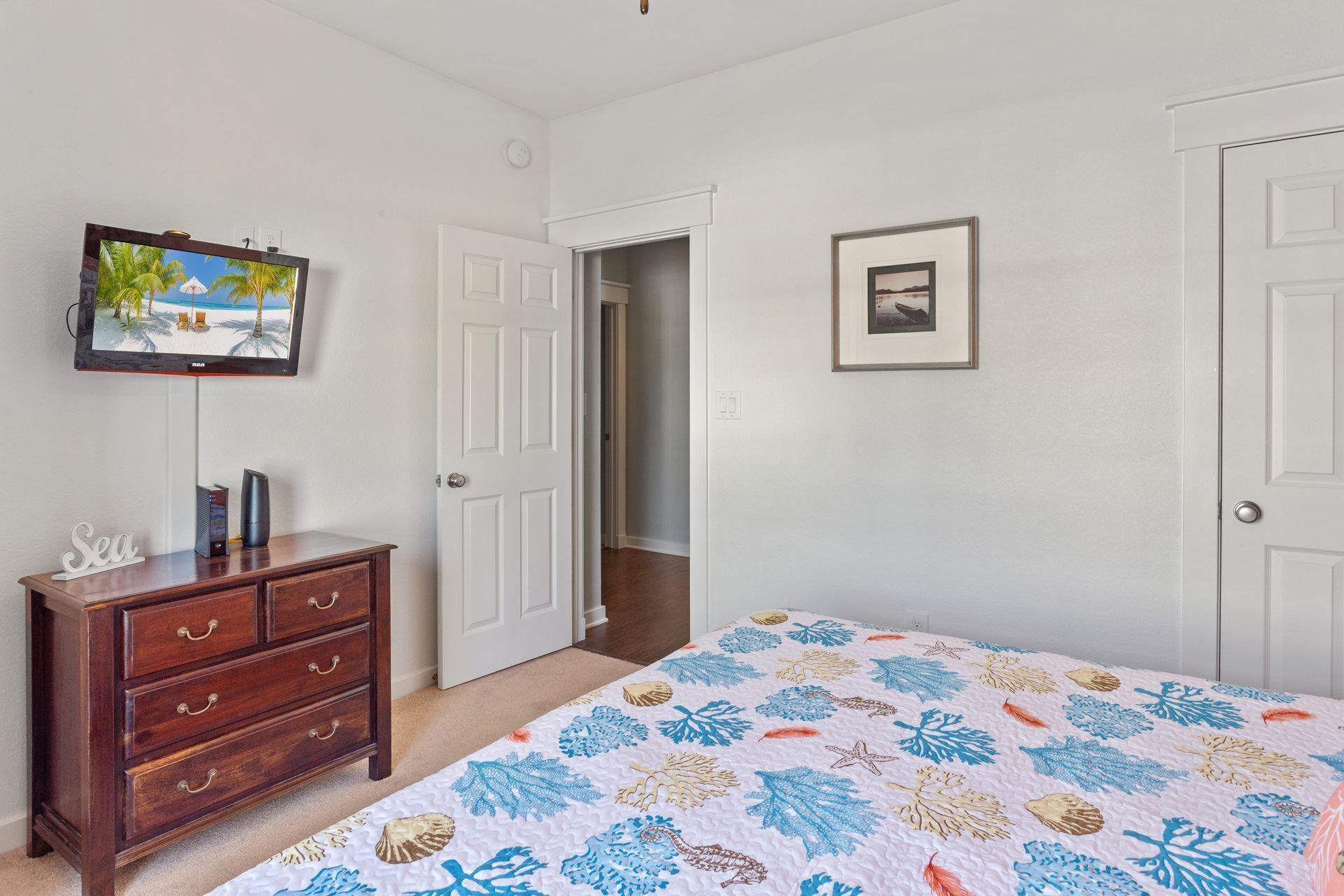 Une chambre à coucher comprenant un lit, une commode, un téléviseur et une porte donnant sur une autre pièce.