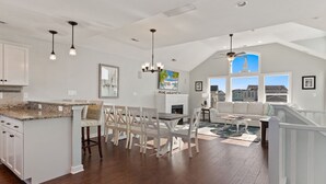 A spacious kitchen with a large island, white cabinetry, and a dining area with a fireplace. - Coastal Luxury | Hot Tub • Game Room • Pool (Corolla)