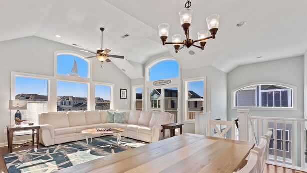 A spacious living room with a large wooden dining table, a white sofa, and a ceiling fan. - Coastal Luxury | Hot Tub • Game Room • Pool (Corolla)