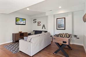 Uma sala de estar com sofá, mesa de futebol, televisão e um quadro na parede.