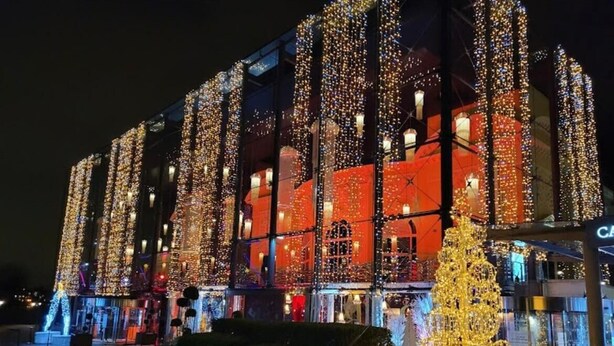 Un immeuble à étages, doté de grandes fenêtres et orné d’un sapin de Noël illuminé devant l’entrée.